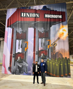 Two men in front of a forging press rendering designed by Macrodyne Technologies.